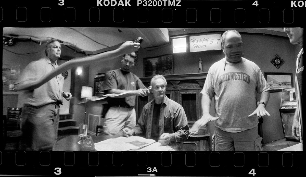 Image showing some of the visual effects that can be achieved with a rotating slit panorama camera like the WideluxX--a man's arm grows across the screen, almost magically while another man's face is heavily distorted by motion.